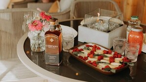 A table set with a bottle of whiskey, a candle, glasses, and a tray of strawberries and raspberries.