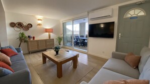 A living room with a sofa, a coffee table, a TV, and a sliding glass door leading to an outdoor patio. - T3 Bord Canal du Midi Piscine (Homps)