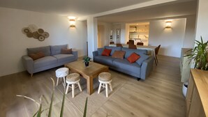 A modern living room with two sofas, a coffee table, and a dining area in the background. - T3 Bord Canal du Midi Piscine (Homps)