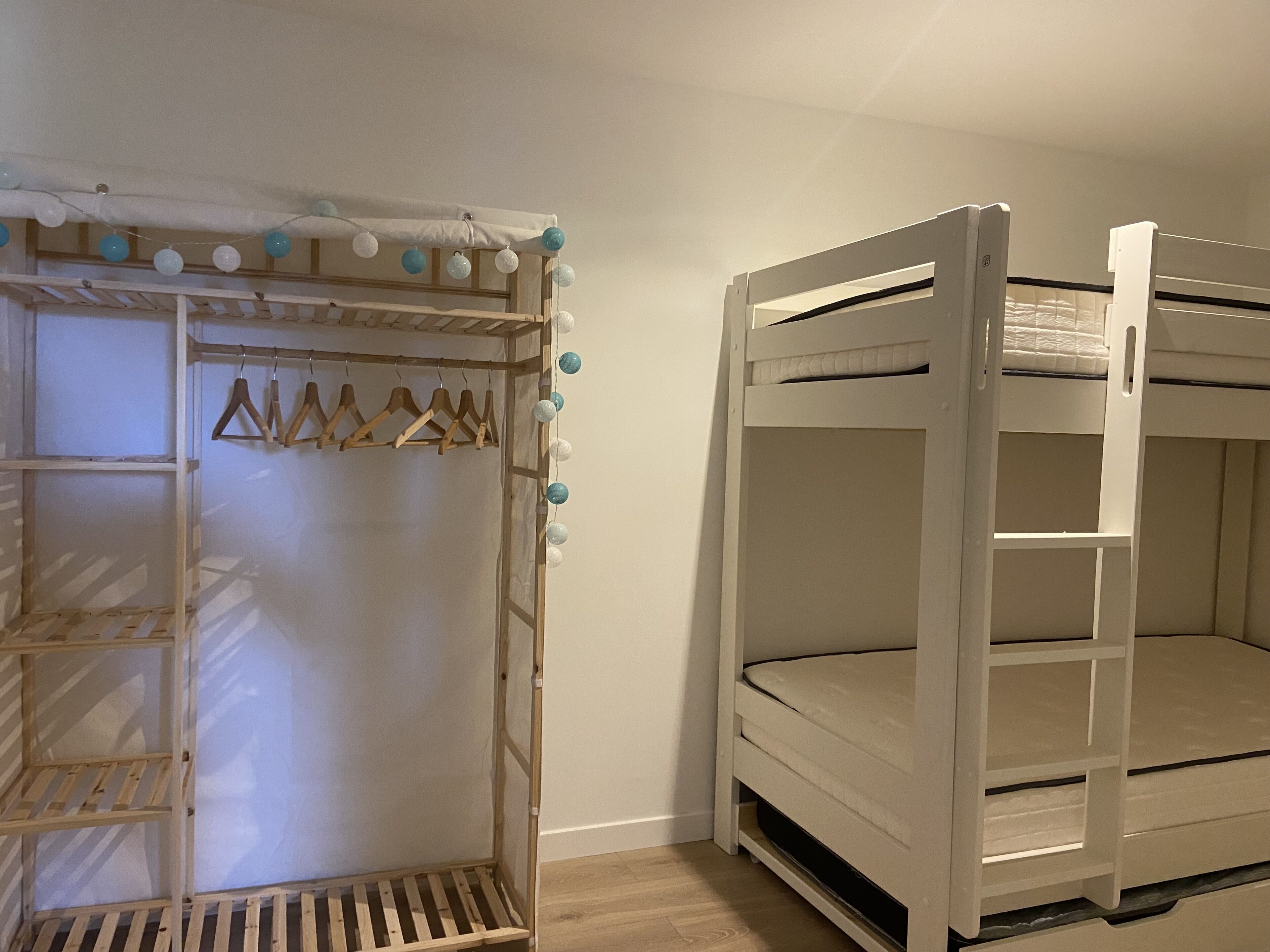 A bunk bed with a wooden ladder and a wardrobe with hanging clothes.