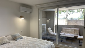 A bedroom with a bed, a sliding glass door leading to an outdoor seating area with a chair and a sofa. - T3 Bord Canal du Midi Piscine (Homps)
