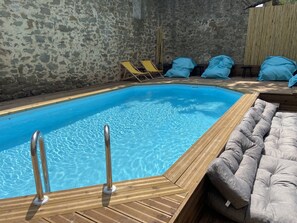 A swimming pool with a wooden deck, lounge chairs, and a cushioned seating area. - T3 Bord Canal du Midi Piscine (Homps)
