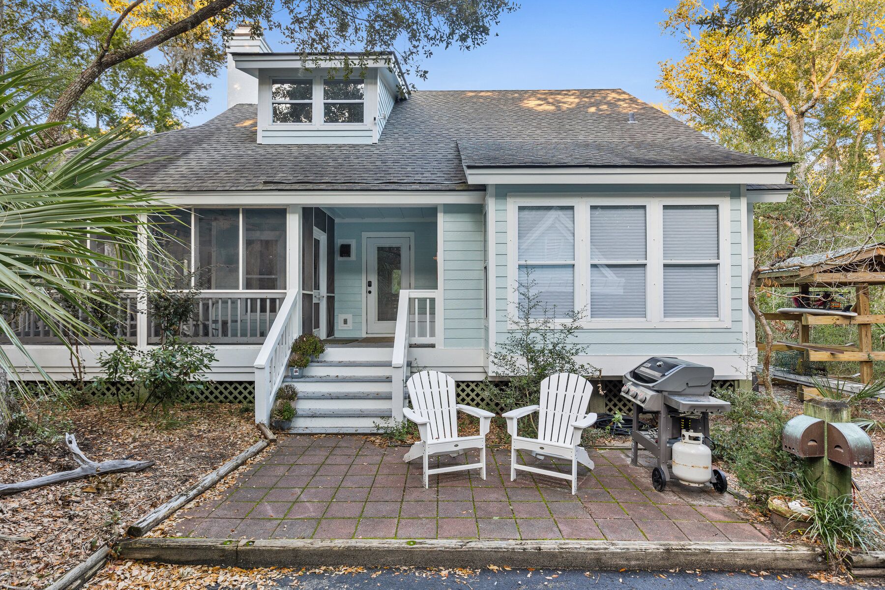 Une maison avec une véranda, deux fauteuils Adirondack, un barbecue et une boîte aux lettres.