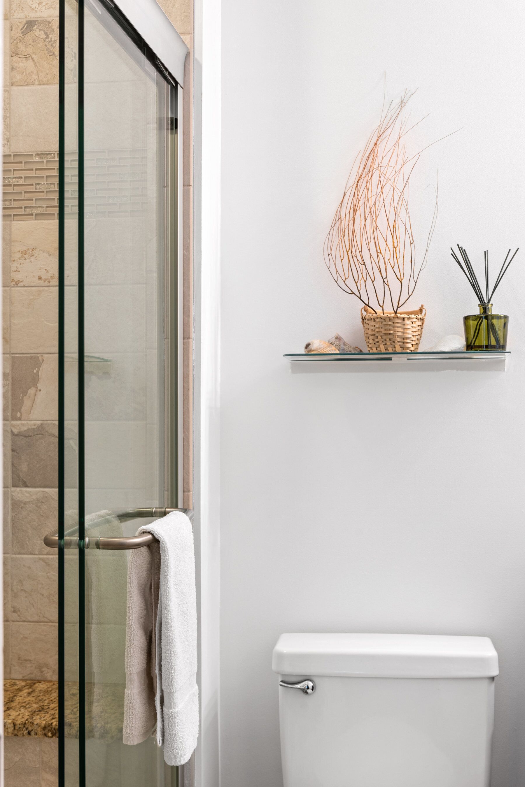 Une salle de bain avec une douche à parois de verre, des toilettes et une étagère ornée d’objets décoratifs.