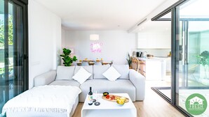 A modern living room with a sofa, a coffee table with food, and a kitchen in the background.