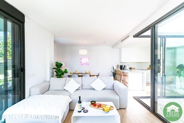 A modern living room with a sofa, a coffee table with food, and a kitchen in the background.