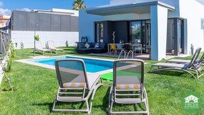 A modern outdoor pool area with lounge chairs, a seating area, and a covered patio.