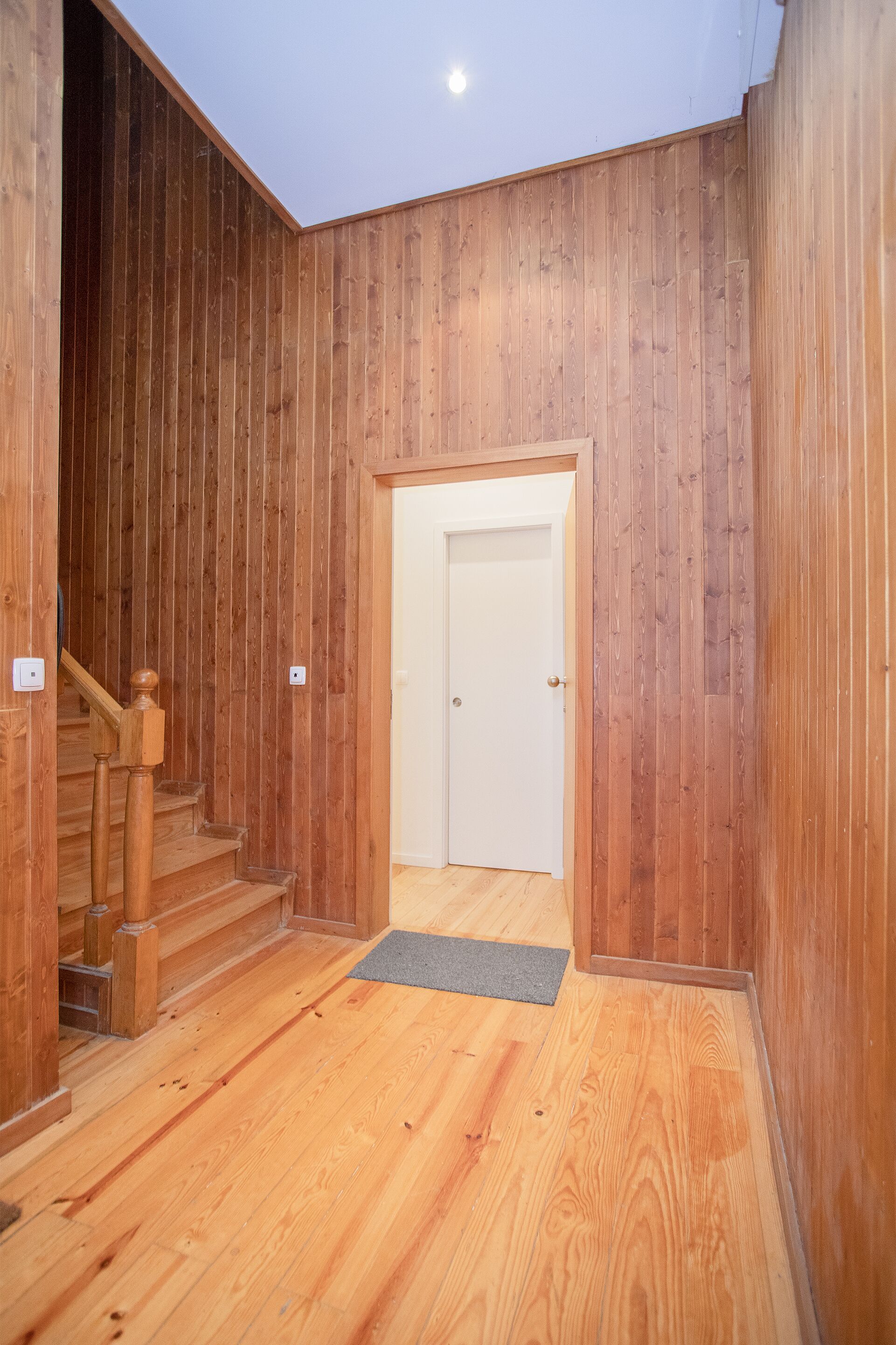 A wooden interior hallway with a staircase leading to a white door.