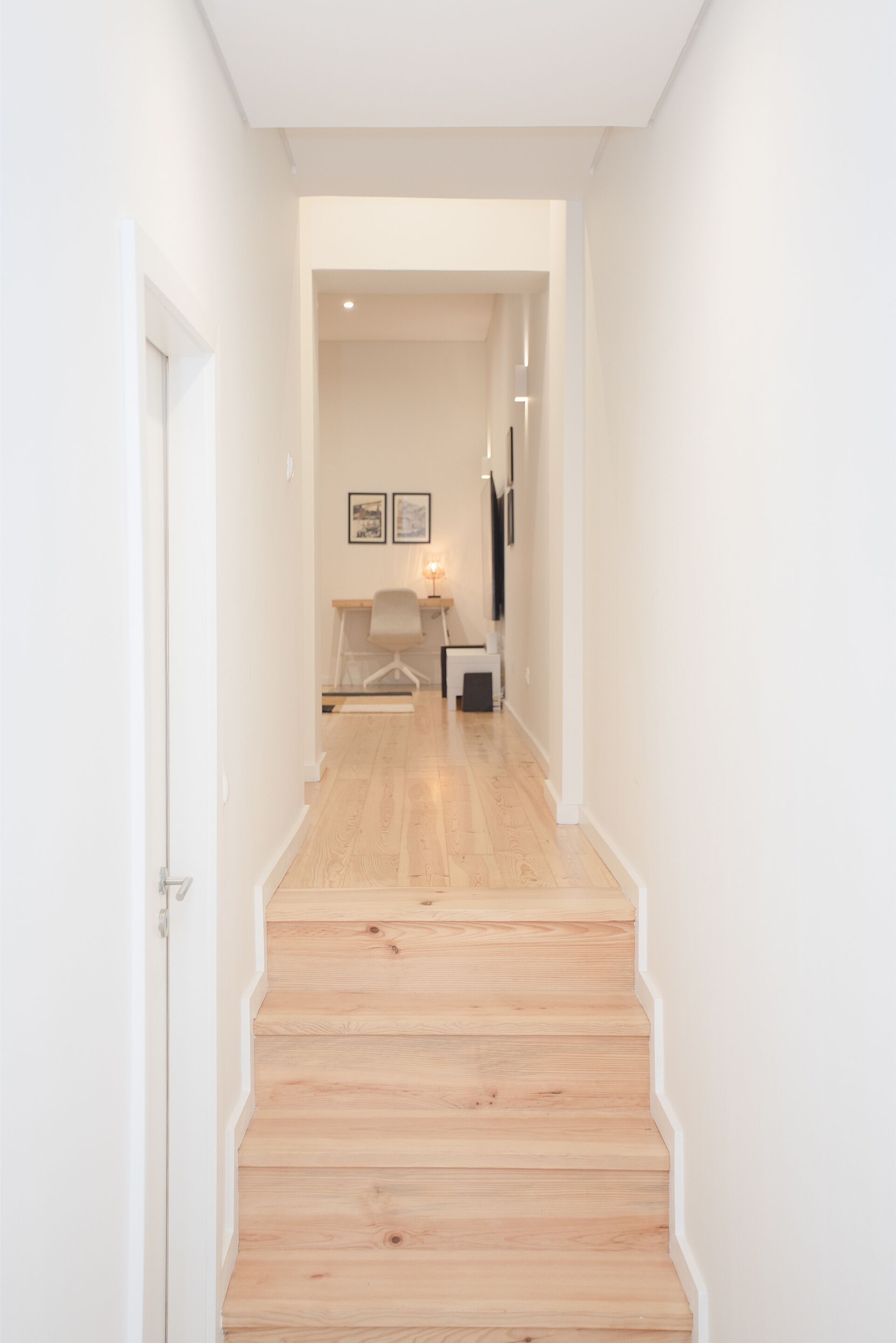 A narrow hallway with wooden stairs leading to a room.