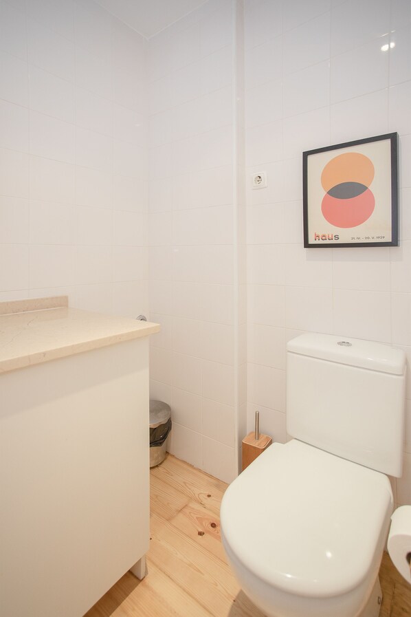 A modern bathroom with a toilet, a sink, and a framed artwork on the wall. - Liiiving - Oasis Retreat Apartment (Porto)