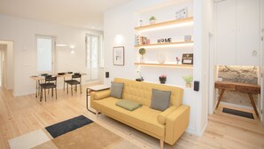 A modern living room with a sofa, dining table, chairs, and a built-in bookshelf with a 'HOME' sign. - Liiiving - Oasis Retreat Apartment (Porto)