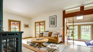 Un salon chaleureux avec une cheminée, un canapé, une table basse et une grande fenêtre donnant sur un paysage verdoyant.