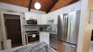 Una cocina con armarios blancos, un refrigerador de acero inoxidable, un microondas y una encimera de mármol.