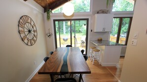 Un comedor con una gran mesa de madera, sillas, un reloj de pared y vistas al exterior a través de un ventanal corredero.