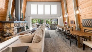 Un intérieur chaleureux avec une cheminée en pierre, un plafond en bois et un coin repas comprenant une grande table et des chaises.