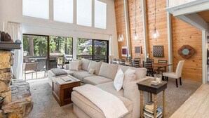 Un salon chaleureux avec un canapé d’angle, une table basse et une chemin ée. De grandes fenêtres et un balcon aménagé avec du mobilier d’extérieur complètent l’ensemble.