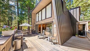 Une maison moderne dotée d’une terrasse, d’un espace salon extérieur et d’une grande fenêtre donnant sur une forêt.
