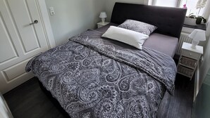 Ein Schlafzimmer mit Bett, Nachttisch, Fenster und Tür.
