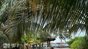 Un sendero pavimentado que conduce a una zona de playa con sombrillas de paja y asientos al aire libre.