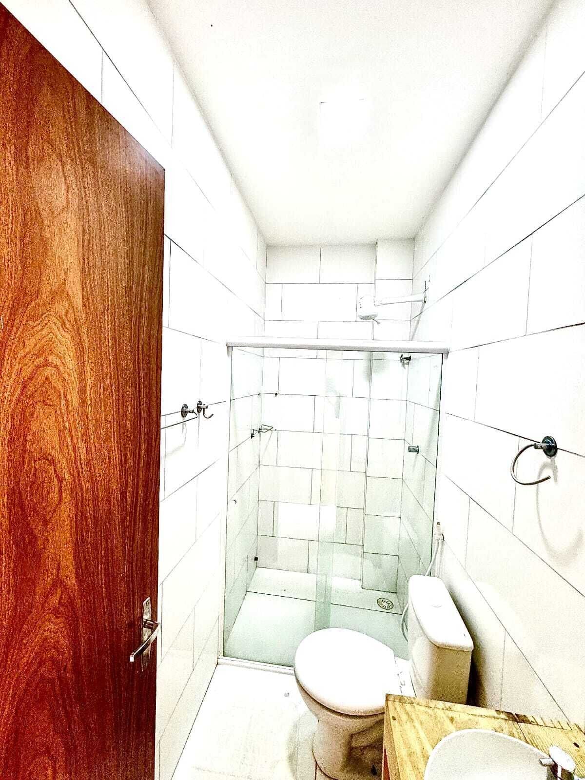 Un baño pequeño y funcional con puerta de madera, cabina de ducha de vidrio, inodoro y lavabo.