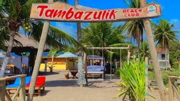 A wooden deck leading to a beach club with palm trees and a clear blue sky.