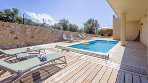 A wooden deck with a pool, lounge chairs, and a stone wall. - Villa Lurenzu - Maison pour 8 avec piscine (Belgodère)