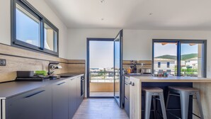 A modern kitchen with a large window, a wooden countertop, and two bar stools. - Villa Lurenzu - Maison pour 8 avec piscine (Belgodère)