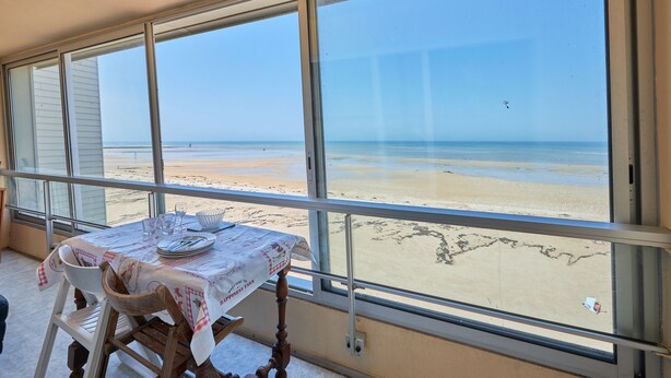 Una stanza con un'ampia finestra vista spiaggia. È apparecchiata una tavola con piatti, bicchieri e tovaglia.