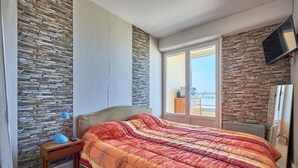Una camera da letto con parete in pietra, un letto con coperta a motivi decorativi, un comodino con una lampada e una TV a parete.