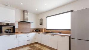 Eine moderne Küche mit weißen Schränken, einem Edelstahlbackofen, einem eingebauten Herd, einer Spüle und einem großen Fenster.