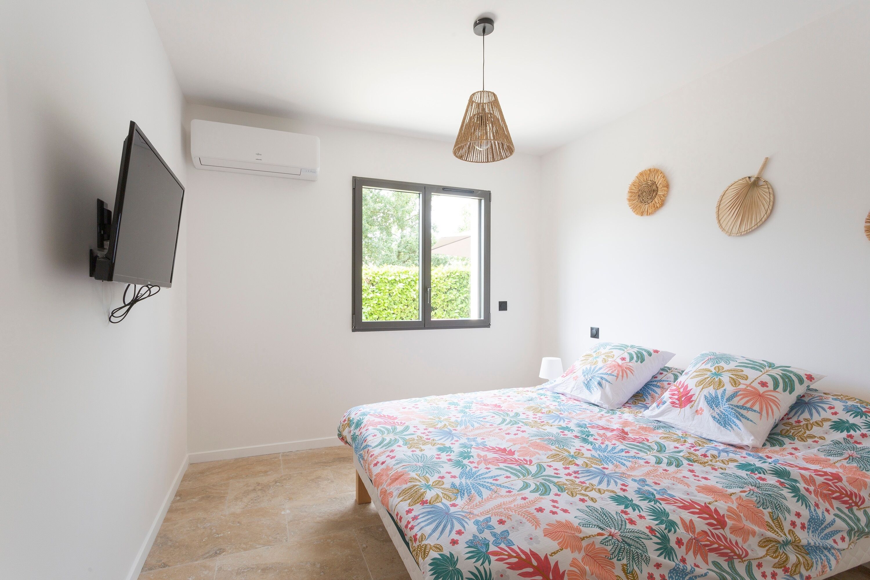 A bedroom with a bed, a TV, a window, and a ceiling fan.