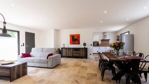 Ein modernes Wohnzimmer mit einer Couch, einem Esstisch für sechs Personen und einer Küche im Hintergrund.
