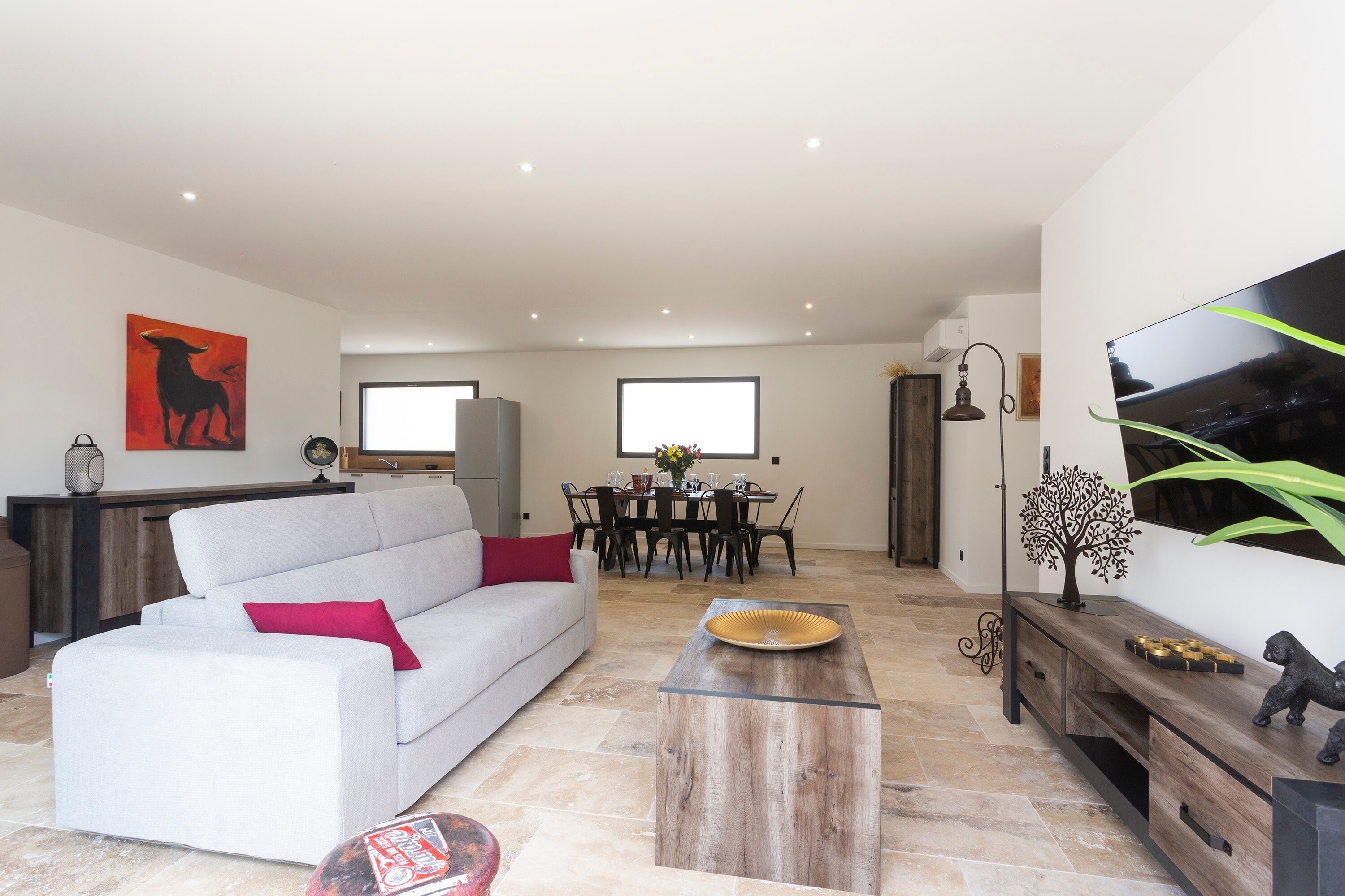 A modern living room with a sofa, a coffee table, a dining area with chairs, and a TV mounted on the wall.