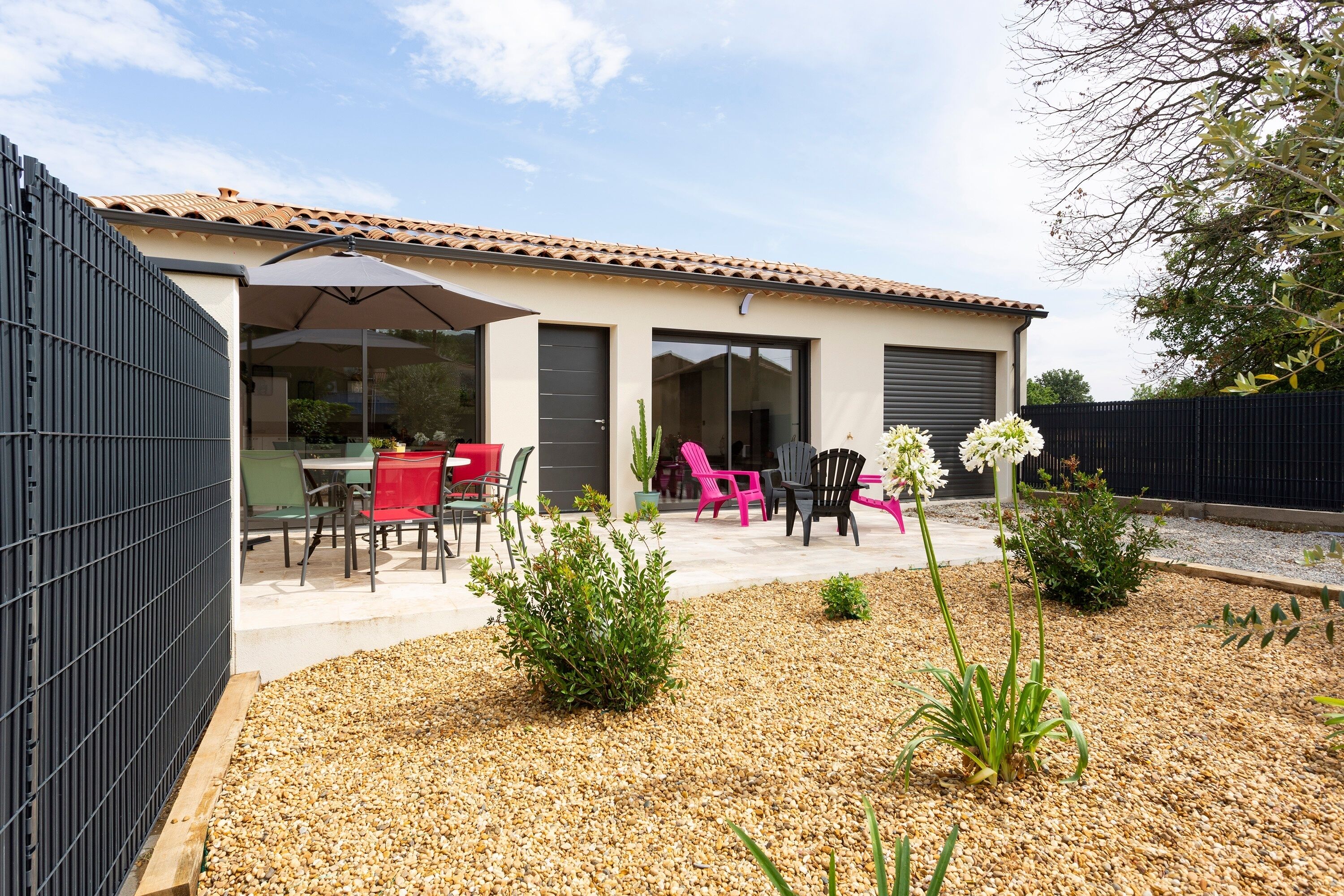 Ein modernes Haus mit einer Terrasse, Gartenmöbeln und einem Garten.