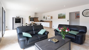 A modern living room with two black leather sofas, a coffee table, and a dining area in the background.