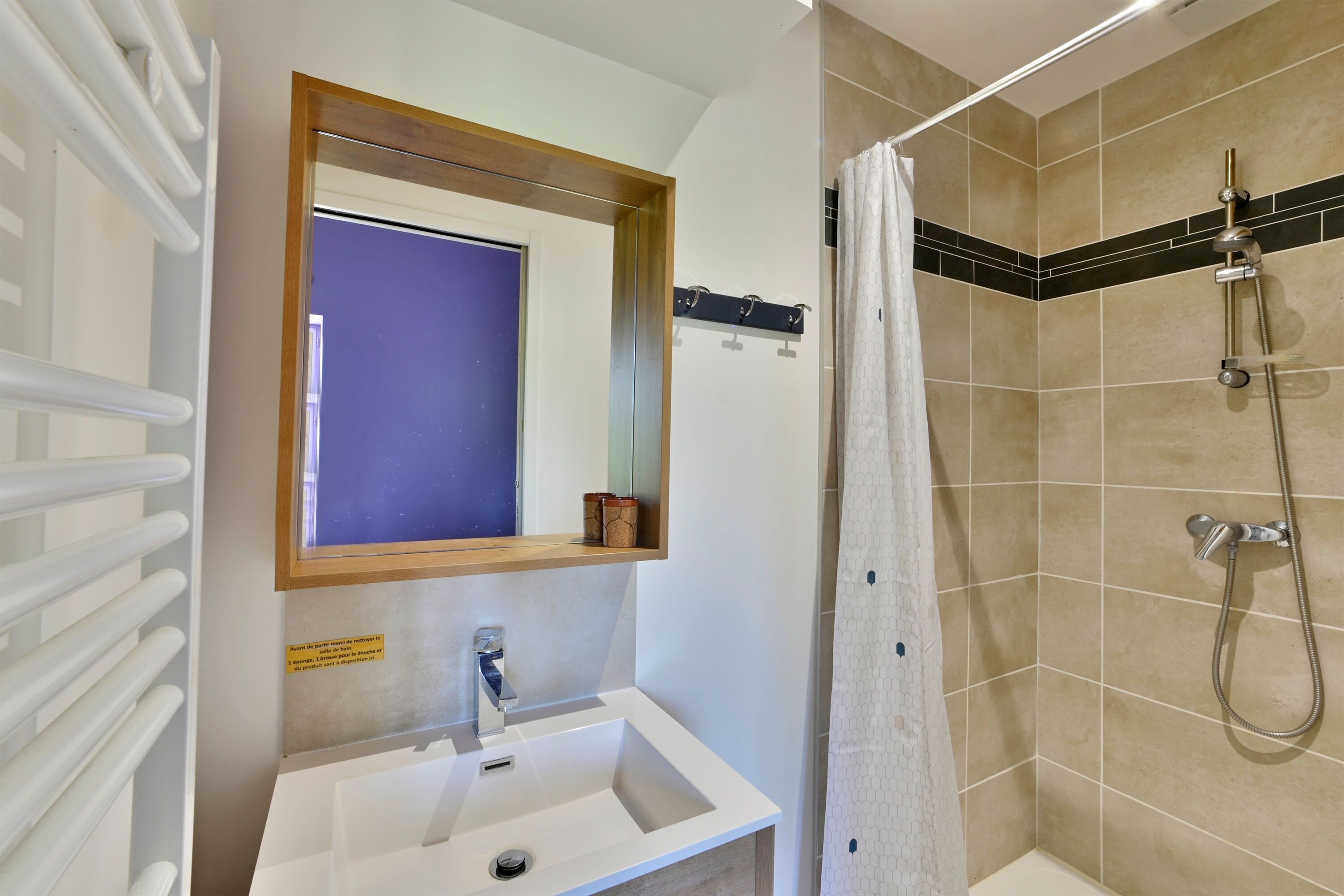 Ein Badezimmer mit einem weißen Waschbecken, einem Spiegel, einer Dusche mit Duschbrause und einem Handtuchhalter.