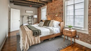 Een slaapkamer met een bakstenen muur, een houten bed, een nachtkastje en een raam met zonwering.