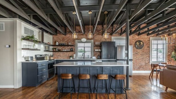 Een ruime keuken met een centraal eiland, barstoelen en een met baksteen beklede wand.