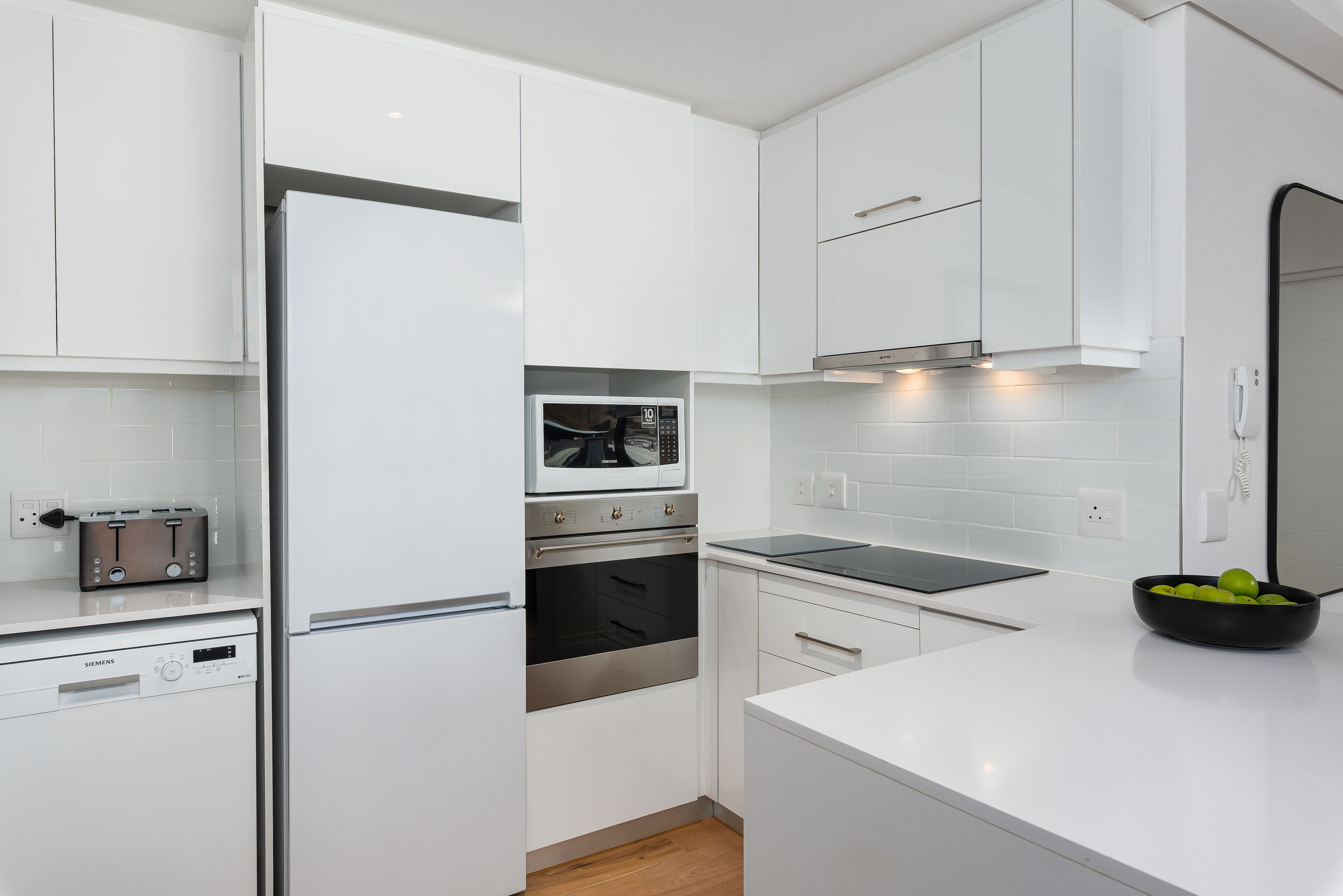 Een moderne keuken met witte kasten, een ingebouwde oven, een magnetron en een vaatwasser.