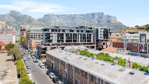 A modern urban street with buildings, a road, and mountains in the background. - Docklands 502 (Cape Town)