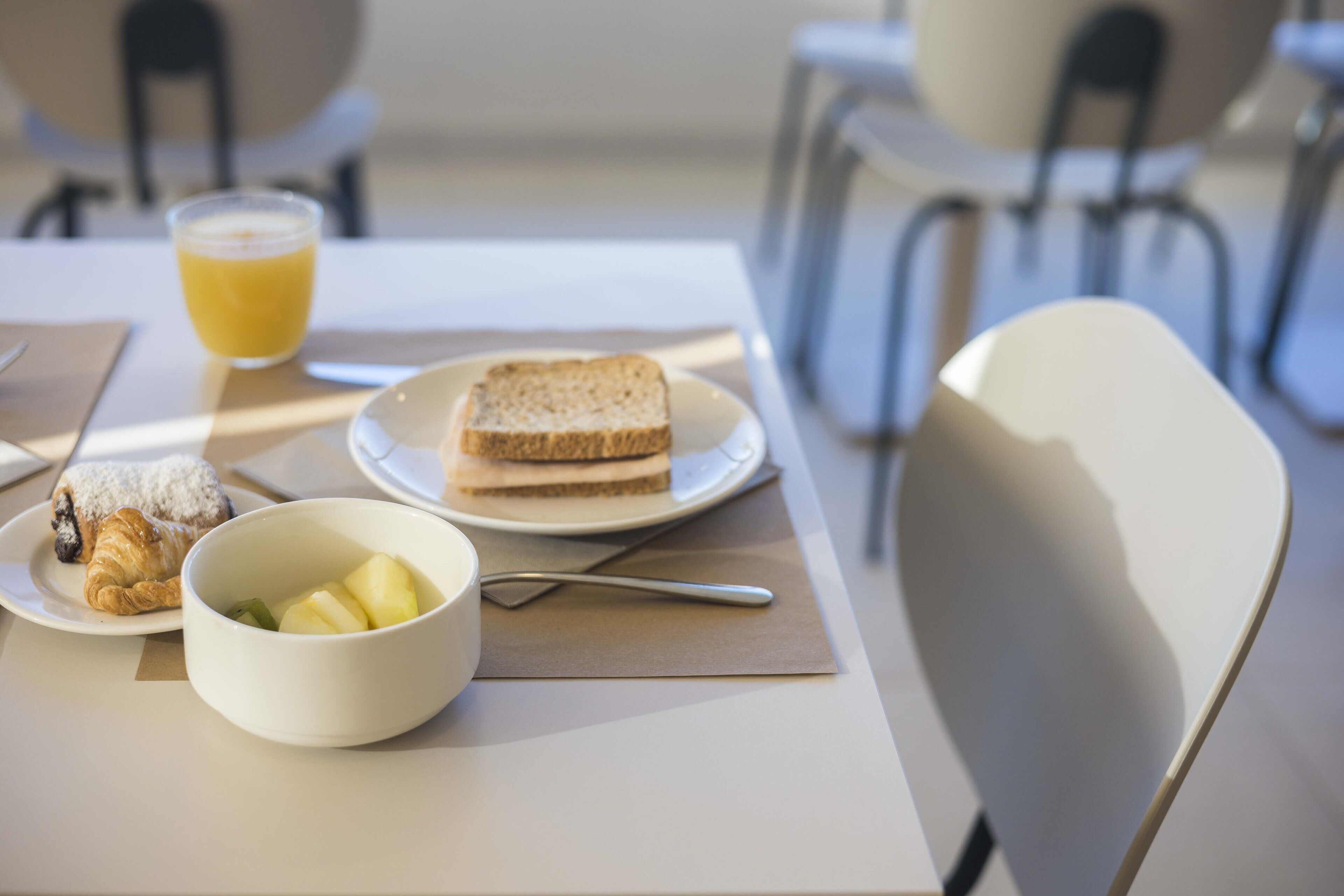 Un desayuno con tostadas, un tazón de fruta, un croissant y un vaso de jugo de naranja sobre una mesa.