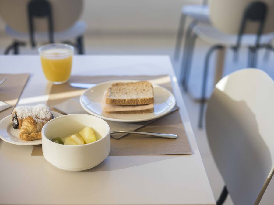 En frukostuppläggning med en tallrik rostat bröd, en skål med frukt, en croissant och ett glas apelsinjuice på ett bord.