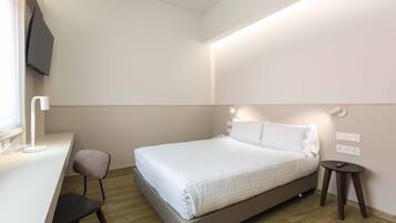 Una habitación de hotel moderna con una cama, un escritorio, una silla y un televisor montado en la pared.