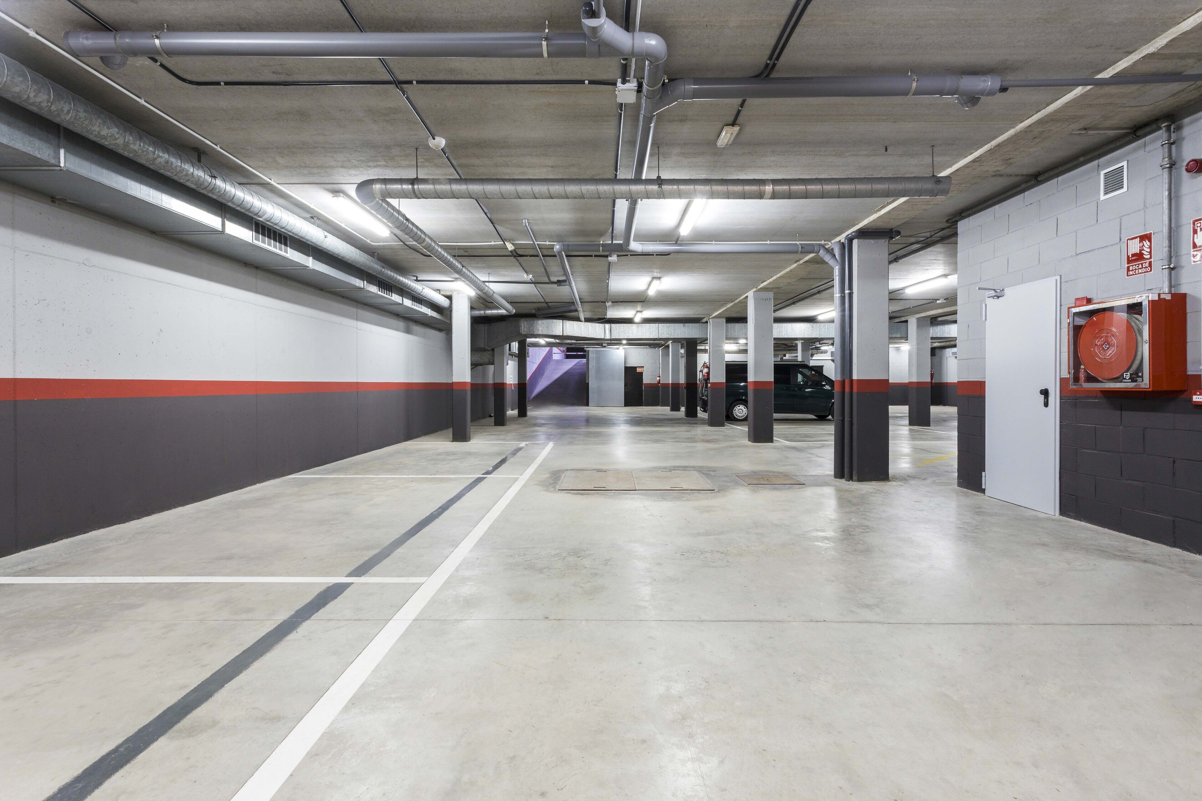 Un parking propre et bien éclairé, avec des murs blancs et gris, une signalisation claire et un extincteur fixé au mur.