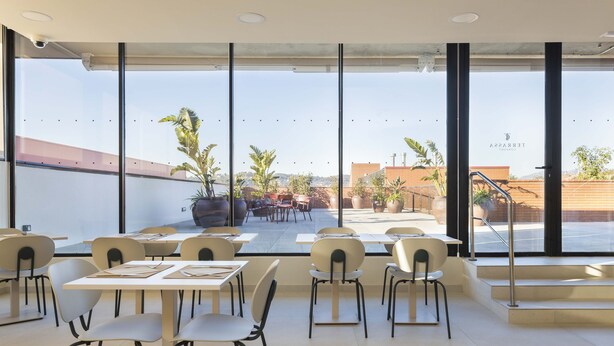 A modern dining area with tables and chairs, large windows offering a view of the outdoors, and a staircase leading outside. - Hotel Terrassa Confort (Terrassa)