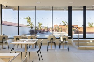 Un comedor moderno con mesas y sillas, ventanas amplias que ofrecen vistas al exterior, y una escalera que da al exterior.