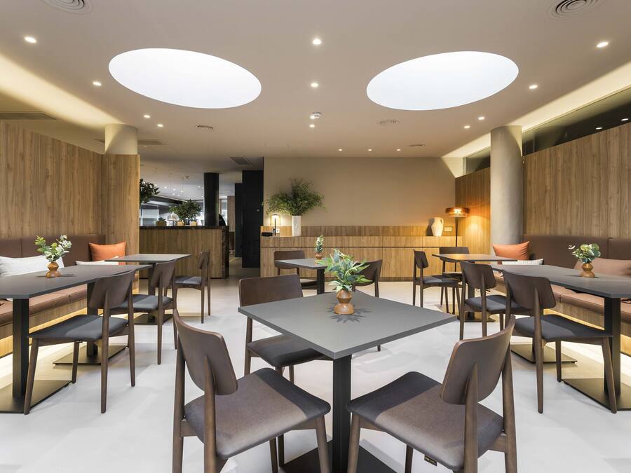 A modern dining area with multiple tables and chairs, wooden panel walls, and recessed ceiling lighting.