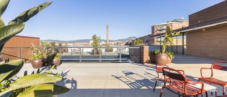 Eine Dachterrasse mit Topfpflanzen, Sitzmöglichkeiten im Freien und Blick auf die Stadtlandschaft.