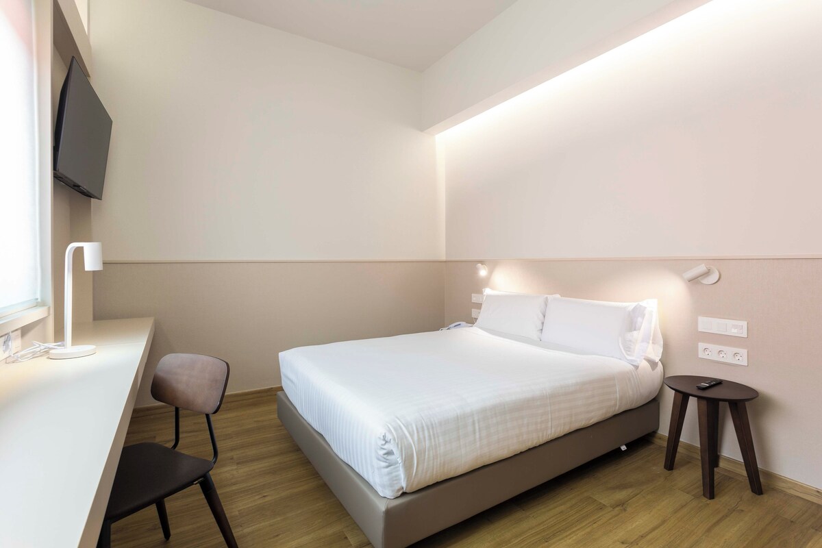 Una habitación de hotel moderna con una cama, un escritorio, una silla y un televisor montado en la pared.