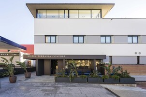 A modern hotel with a flat roof, large windows, and a sign reading "HOTEL TERRASSA CONFORT".